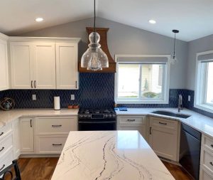 Kitchen_Remodeling_St-Paul-MN Kitchen remodeling project with white cabinets and a white marble countertop and a blue chevron tile backsplash with the same blue color cabinets on the island and a dark wooden hood vent over the stove. Kitchen remodeled by Carter Custom Construction