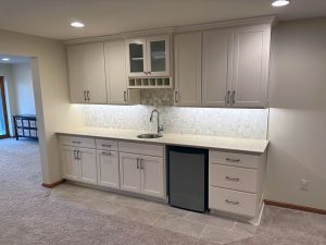 basement-remodel-wetbar_lakeville_mn Built in home bar with white cabinets, dishwasher and sink, and a white and gray subtle backsplash, built by Kitchen remodel with open shelving and white cabinets, by Carter Custom Construction