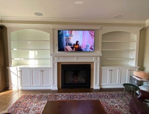 custom built white mantel, cabinetry, and shelving surrounding a gas fireplace, all built by Carter Custom Construction