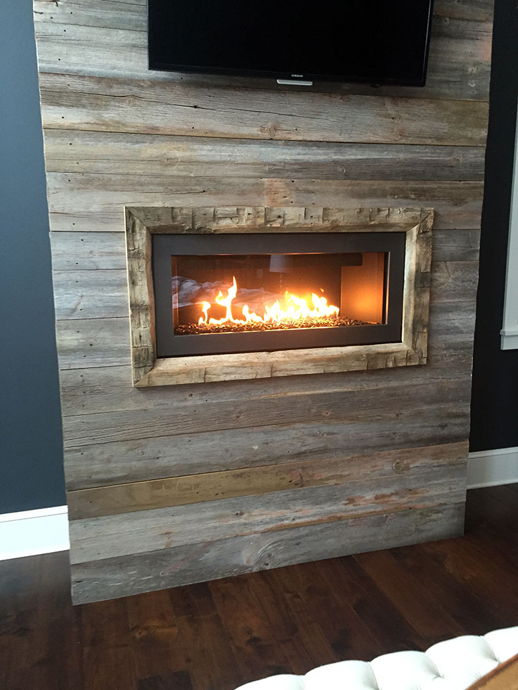Gas fireplace with a rustic wood mantel and dark accent wall, completed by Carter Custom Construction.