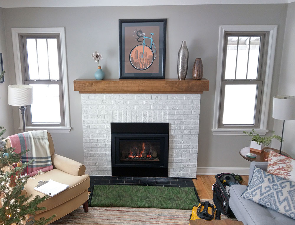 Cozy living room with a white brick fireplace, wooden mantel, and modern decor, completed by Carter Custom Construction.