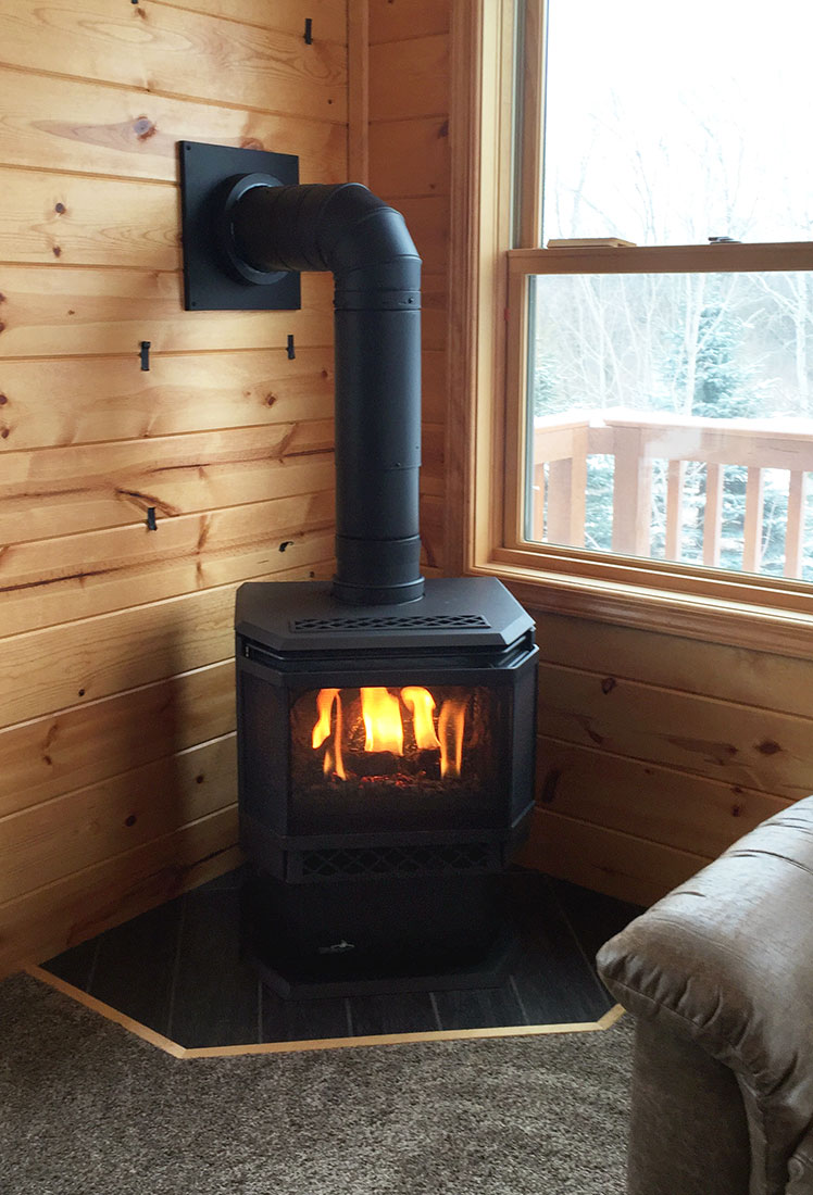 Small wooden stove in the corner of a cabin. Installed by Carter Custom Construction, your trusted builder for fireplaces and stoves.