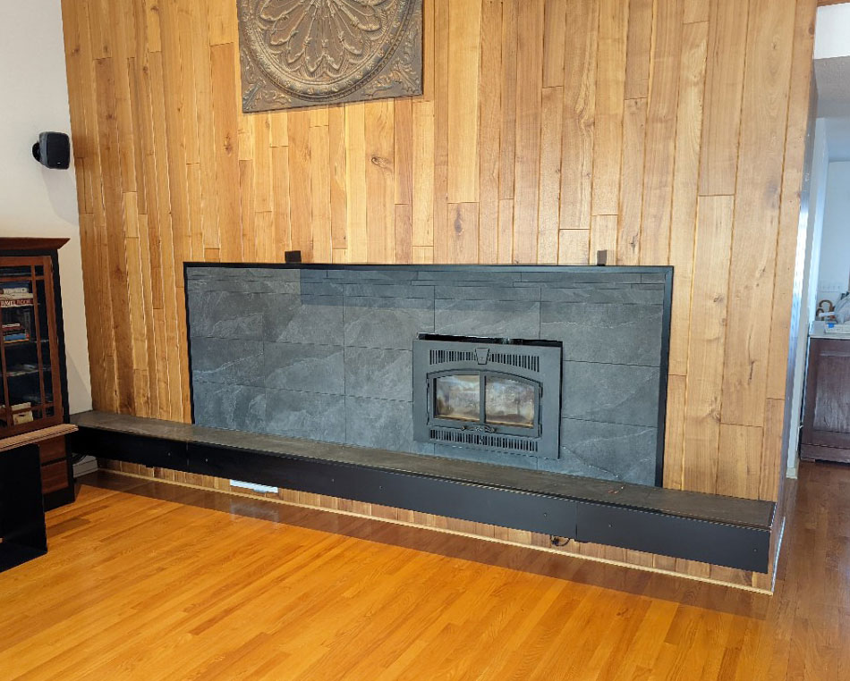 Living room with a wood-paneled wall and a black slate fireplace insert, completed by Carter Custom Construction.