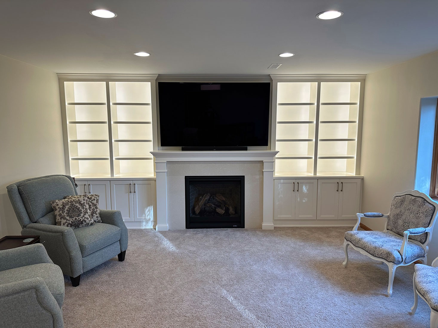Large light up white bookshelves and custom built cabinets surrounding a traditional fireplace and mantels, built by Carter Custom Construction