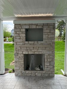 Large outdoor fireplace surround with cream stone and mantels ledge, built by Carter Custom Construction