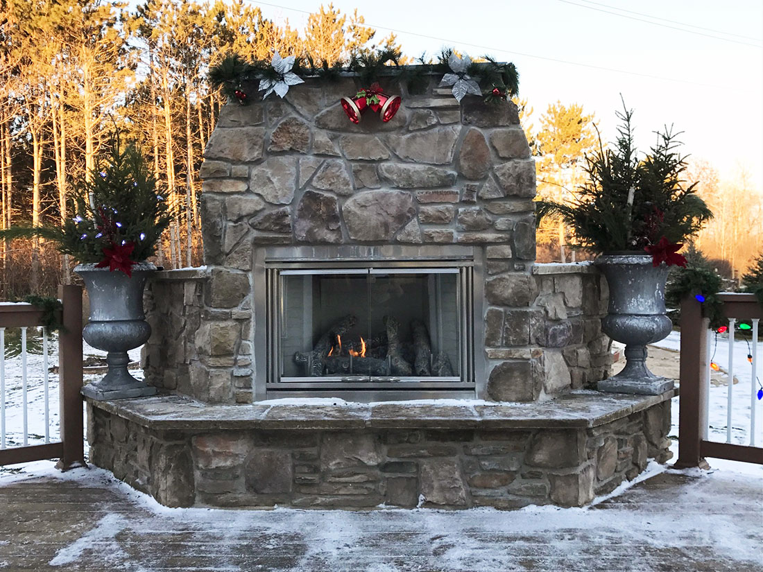 Outdoor stone fireplace decorated for the holidays with greenery and ornaments, completed by Carter Custom Construction.