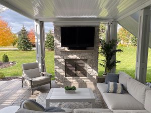 exterior-fireplace-sitting-area_twin-cities_mn open porch under deck with fireplace built in with TV and sitting area, built by Carter Custom Construction