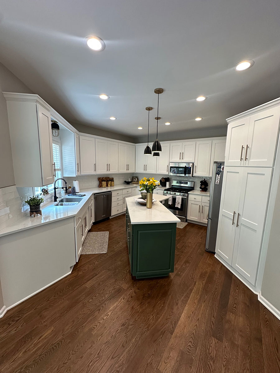 Modern kitchen with white cabinets and a large island with dark forest green cabinets and a white marble countertop, remodel built by Carter Custom Construction