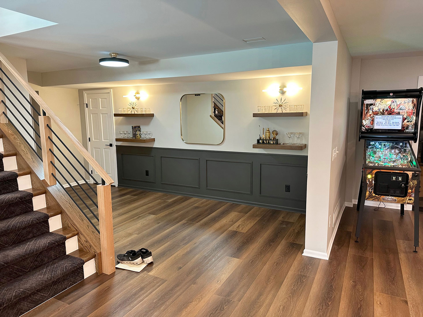 Beautifully finished basement with modern lighting, dark wood flooring, a stylish staircase, and a pinball machine, completed by Carter Custom Construction