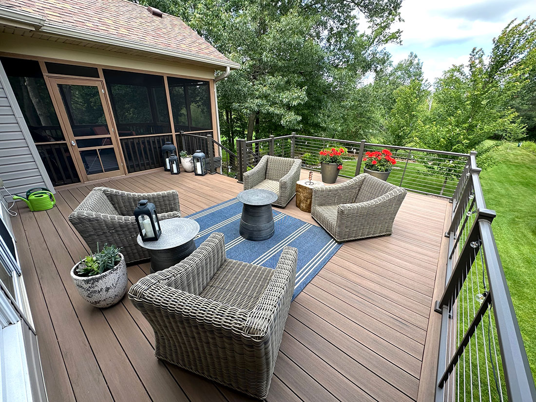 Spacious outdoor deck with wicker furniture and a view of lush greenery, completed by Carter Custom Construction.